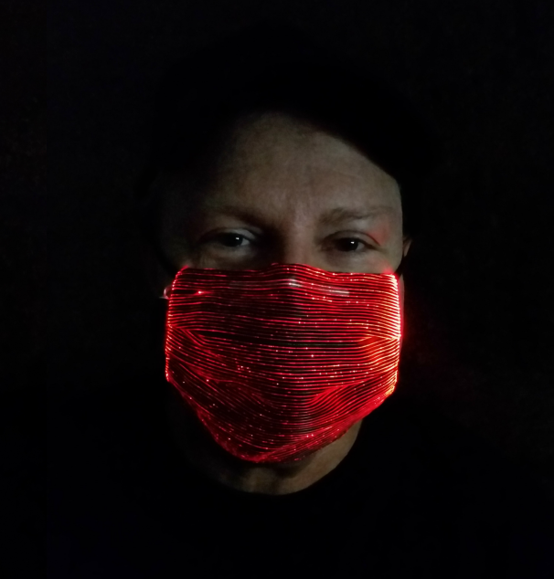 Guy wearing a glowing red LED mask in the dark.