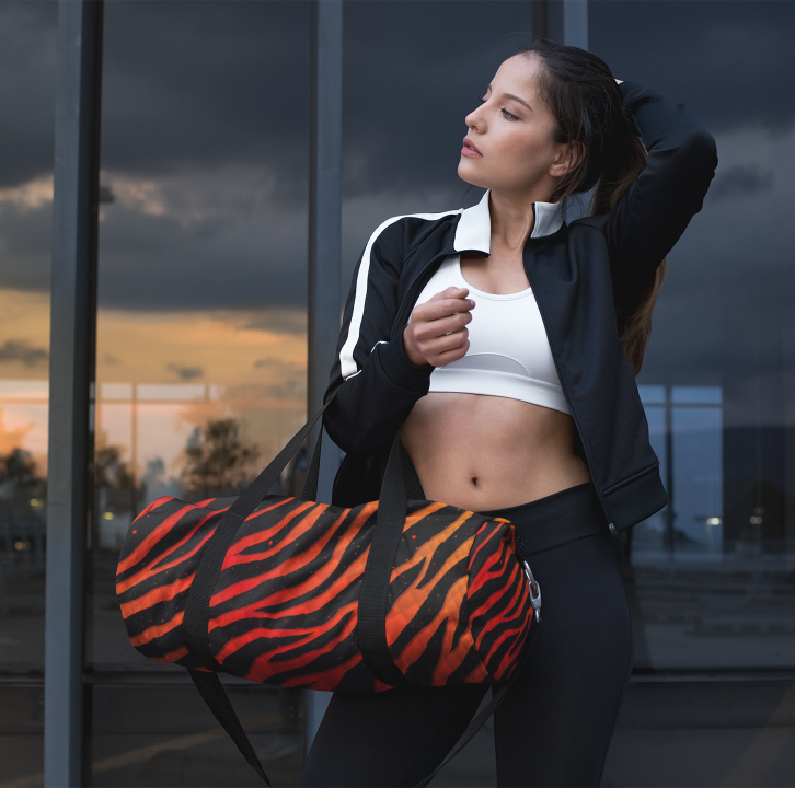 Woman holding an orange/red Ripped Spacetime Stripes duffel bag.