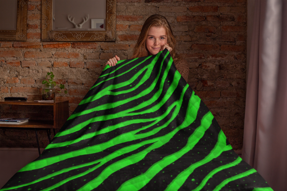 Woman sitting under a green Ripped Spacetime Stripes throw blanket.