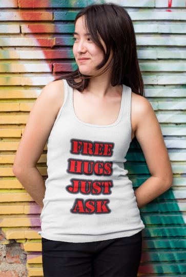 Woman wearing a Free Hugs Just Ask white tank top leaning against a rainbow brick wall.